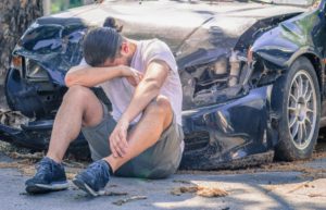 Man sitting in front of his damaged car