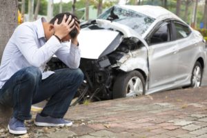 Disappointed man sitting near his damaged car