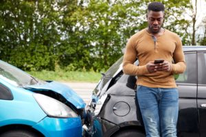 Men standing with damaged cars using his mobile phone