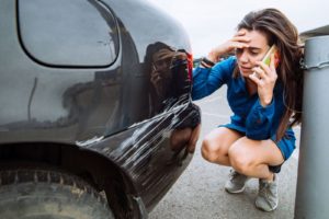 A girl taking on mobile sitting on road near her car with scratches