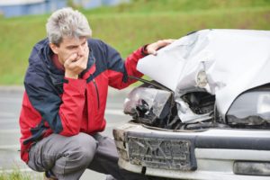 Worried man looking at his damaged car after accident