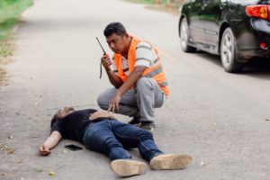 An injured man lying on the road while a rescue worker calling on walkie talkie sitting near him